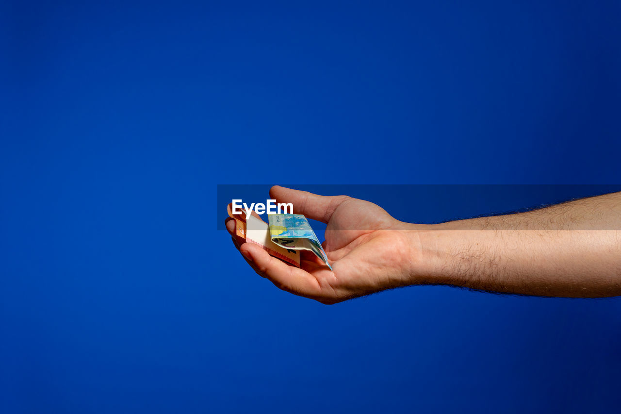 Cropped hand of man holding banknotes against blue background