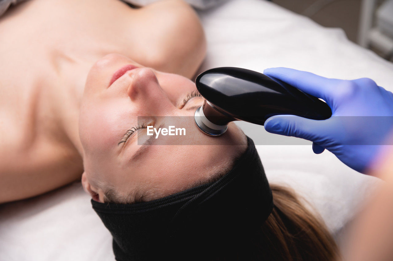 Young woman undergoing facial rejuvenation procedure with tekar therapy in salon, top side view