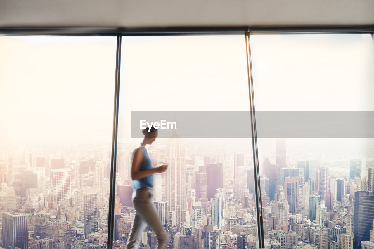 Side view of woman by glass window against buildings in city