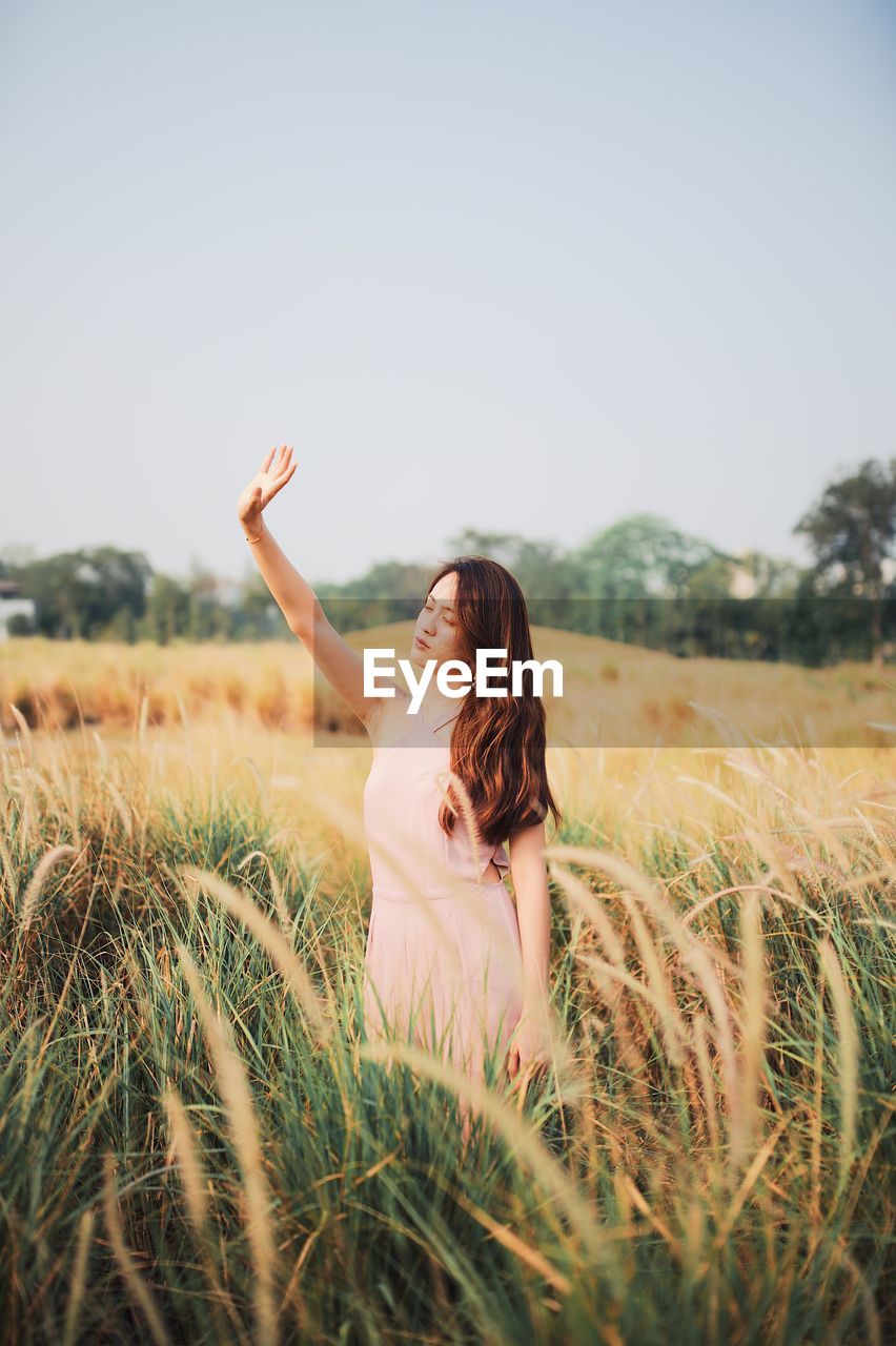 Beautiful woman with arms raised standing on field against sky