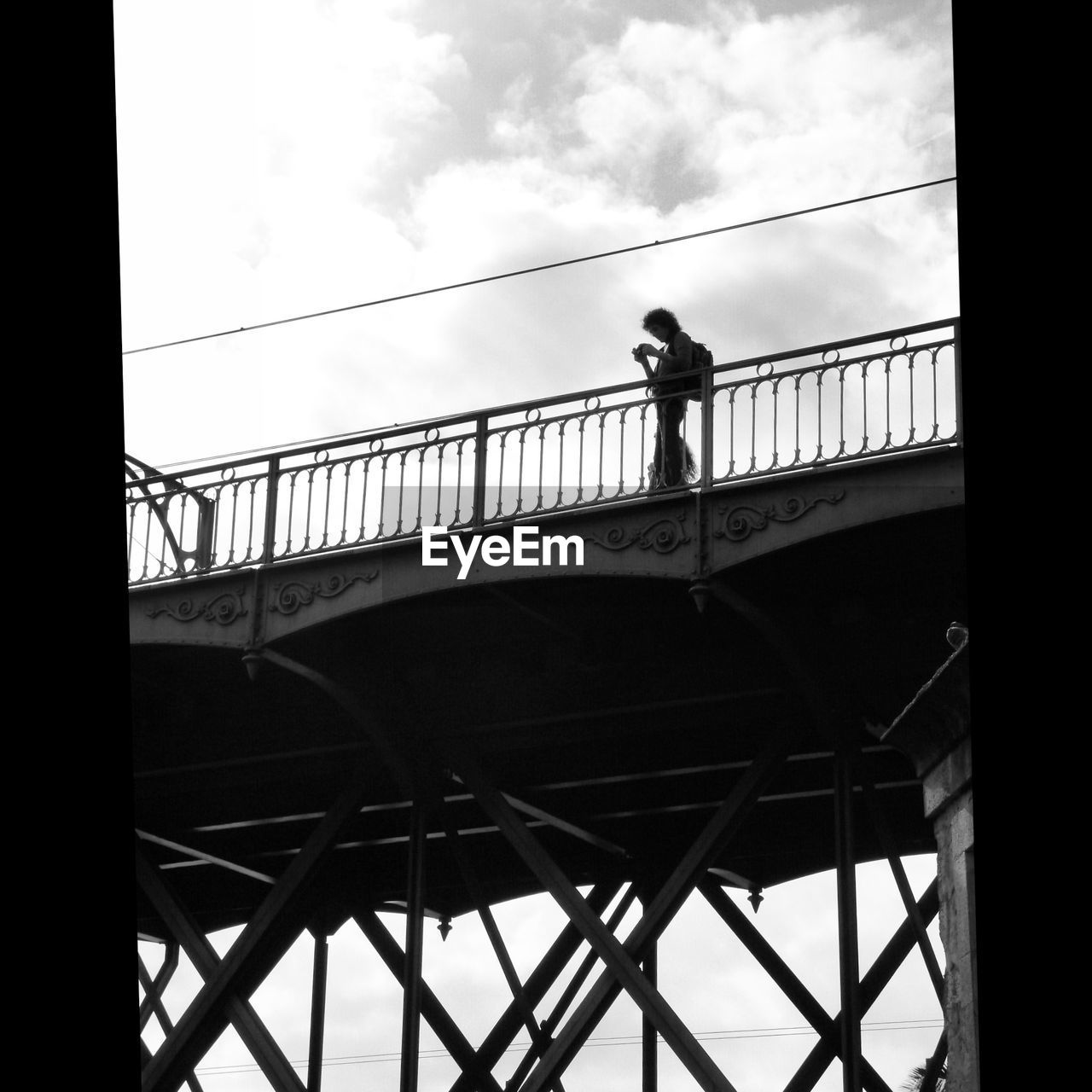 Low angle view of woman standing on bridge against cloudy sky