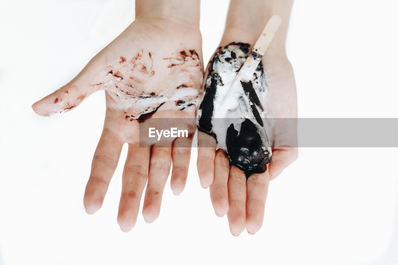 Cropped hands with melted ice cream against white background