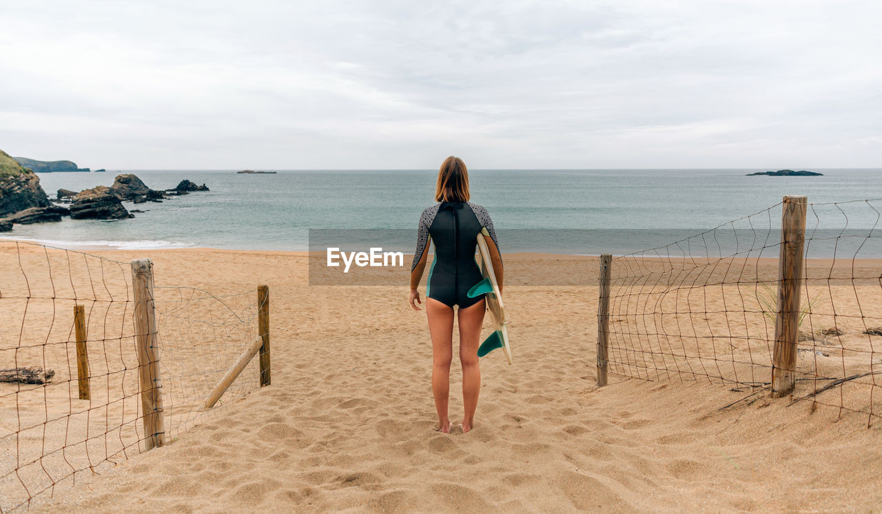 Surfer woman with wetsuit and surfboard looking at the sea