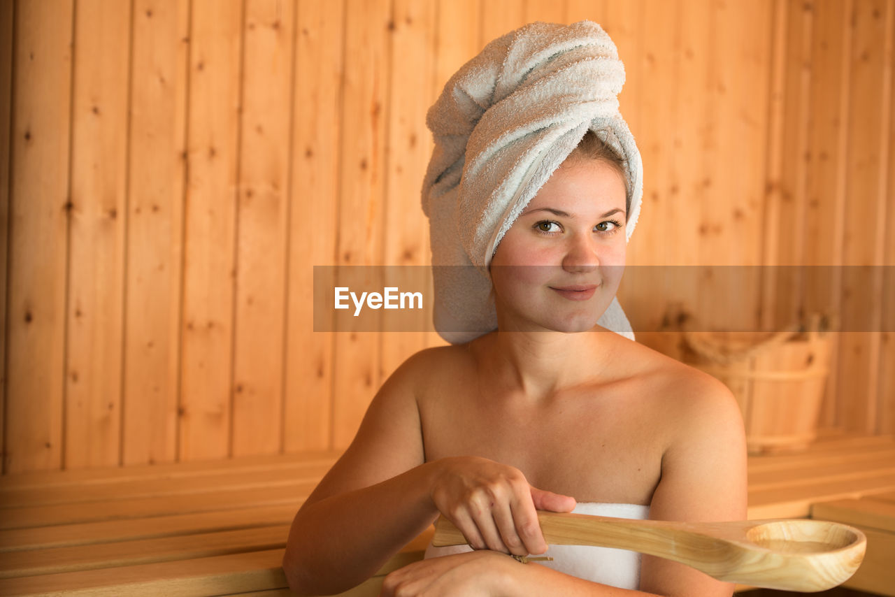 Beautiful young woman holding wooden spoon while sitting in sauna