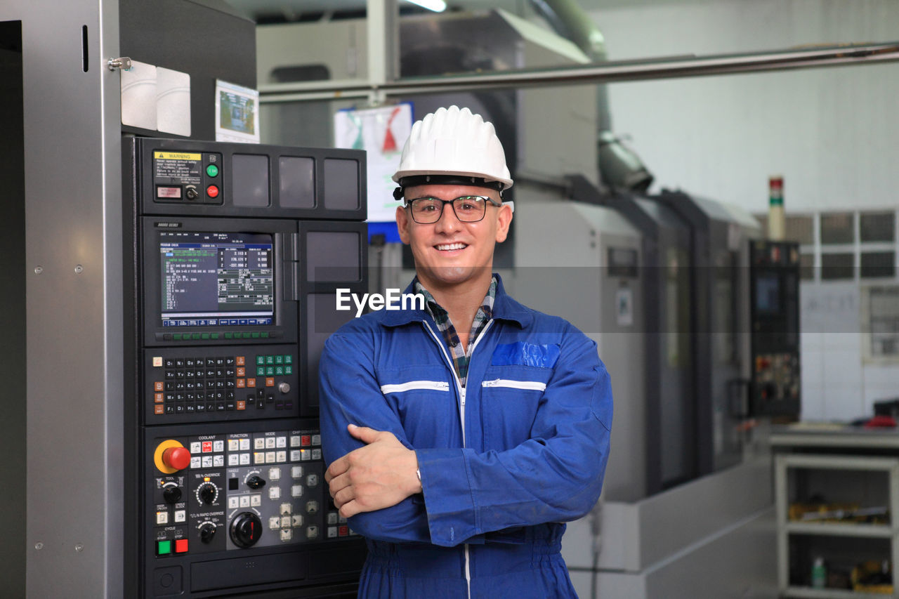 PORTRAIT OF SMILING MAN STANDING IN FACTORY