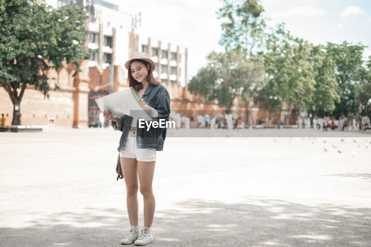 FULL LENGTH PORTRAIT OF YOUNG WOMAN STANDING ON CITY IN BACKGROUND