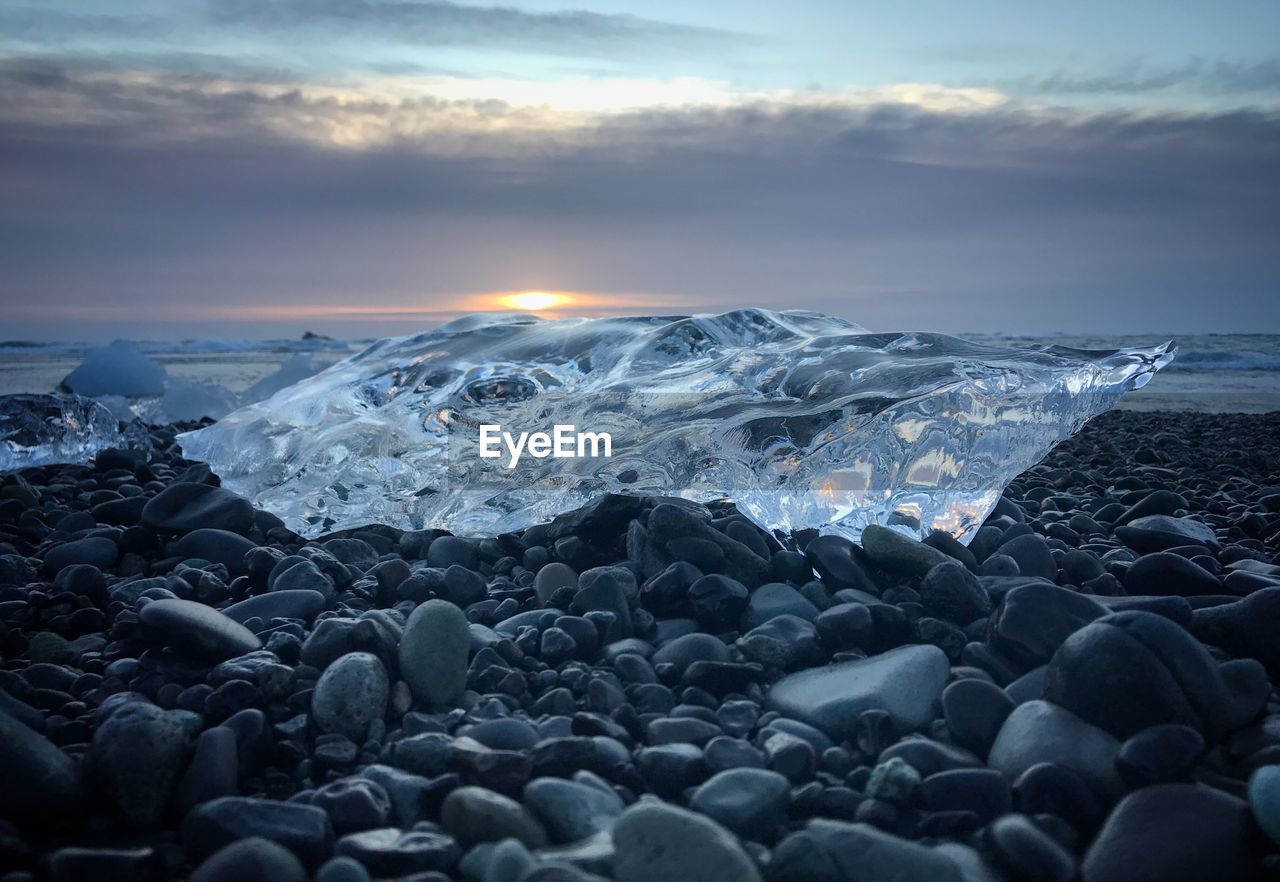 Close-up of pebbles at beach against sky during sunset