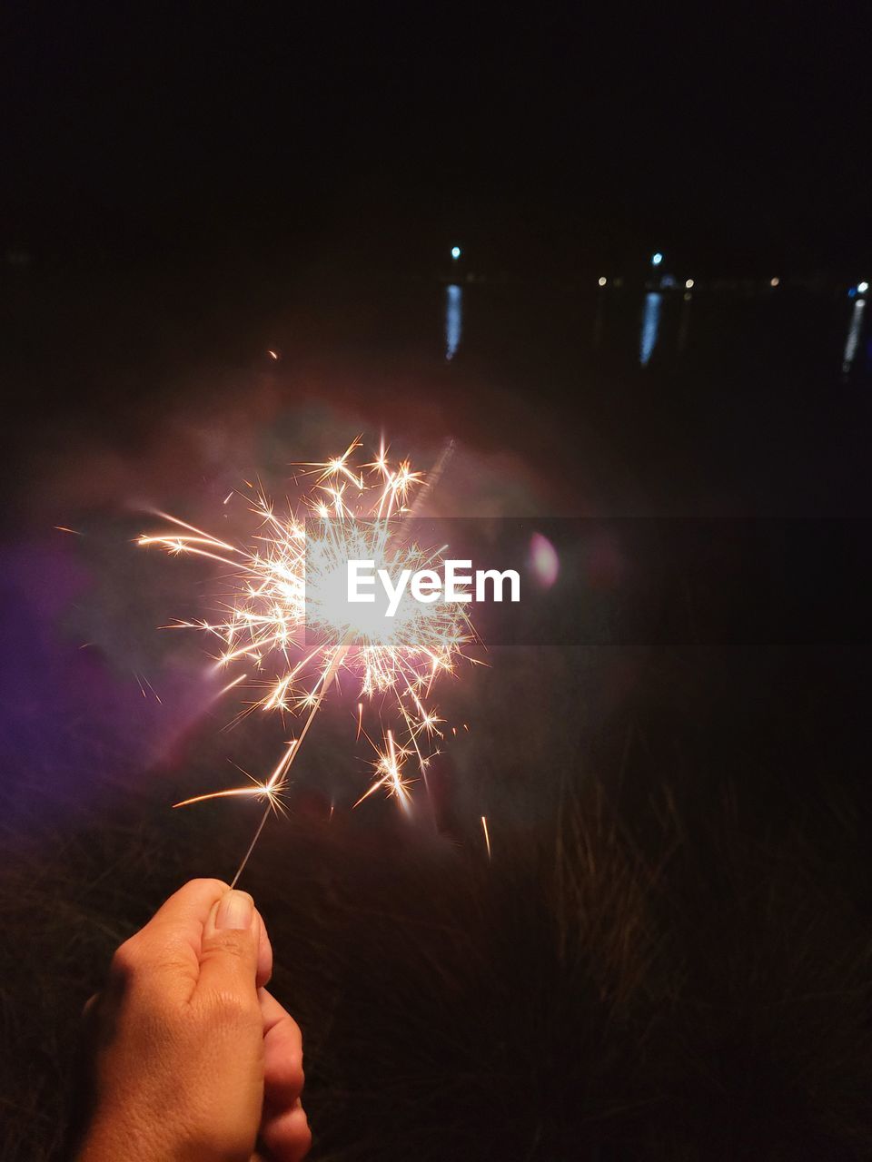 LOW ANGLE VIEW OF HAND HOLDING ILLUMINATED FIREWORK DISPLAY