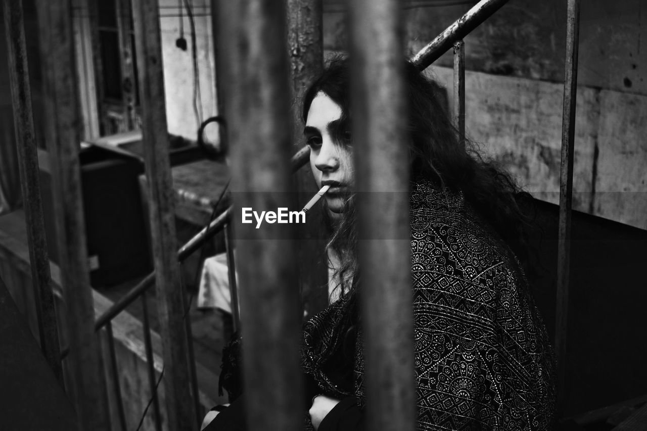 Young woman smoking cigarette seen through railing