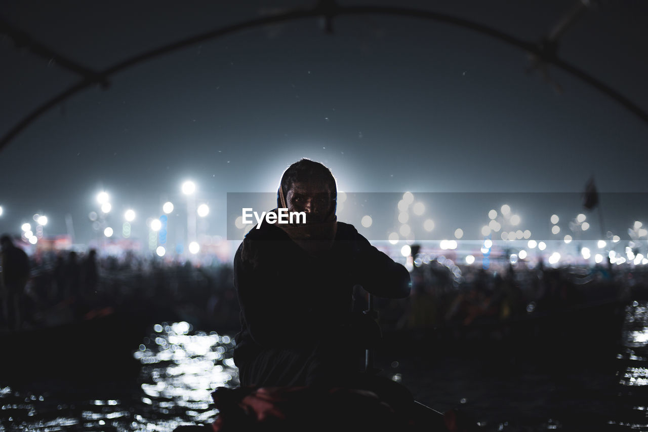 MAN STANDING BY ILLUMINATED LIGHT AT NIGHT