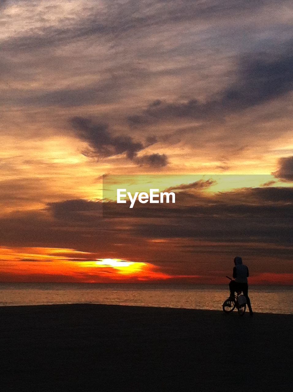 Man on bicycle on beach at sunset