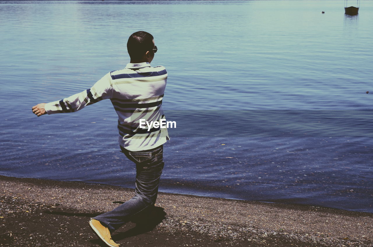 Rear view of man standing at lakeshore on sunny day