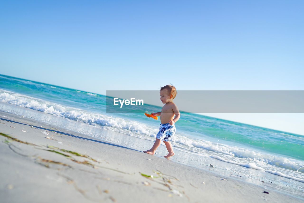 Shirtless boy walking on shore against sky