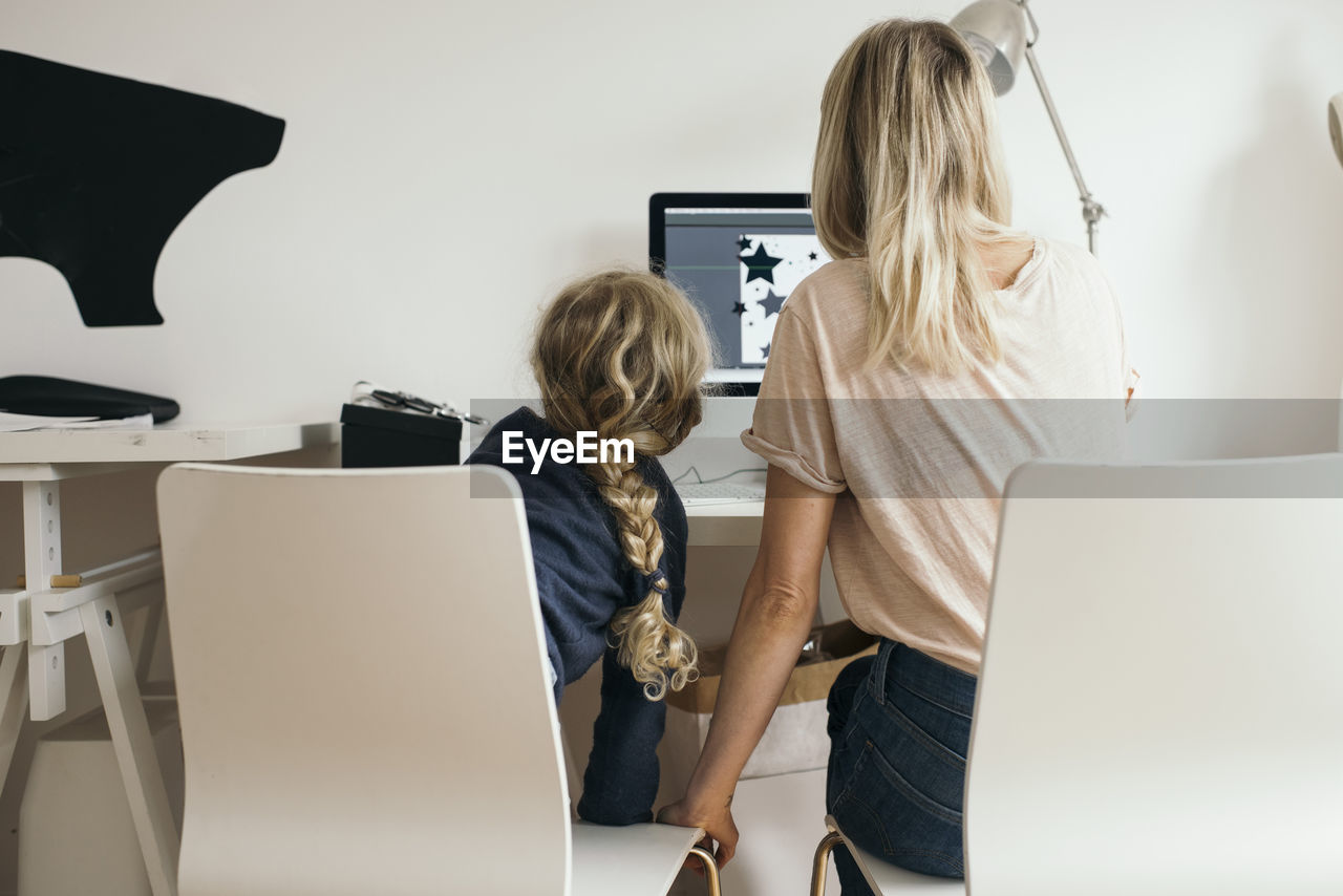 Rear view of girl with mother using laptop at home