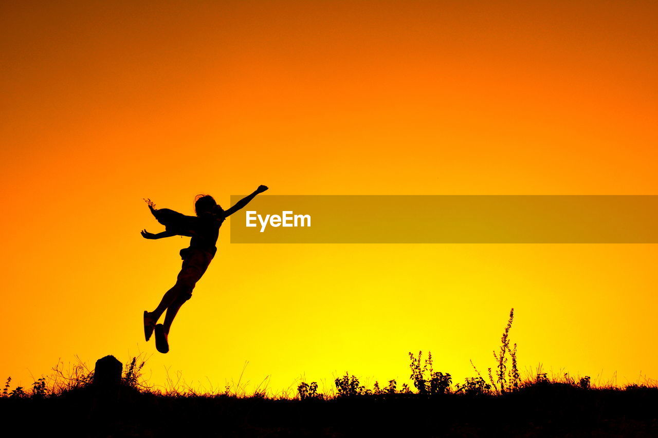 Silhouette person jumping in mid-air against orange sky