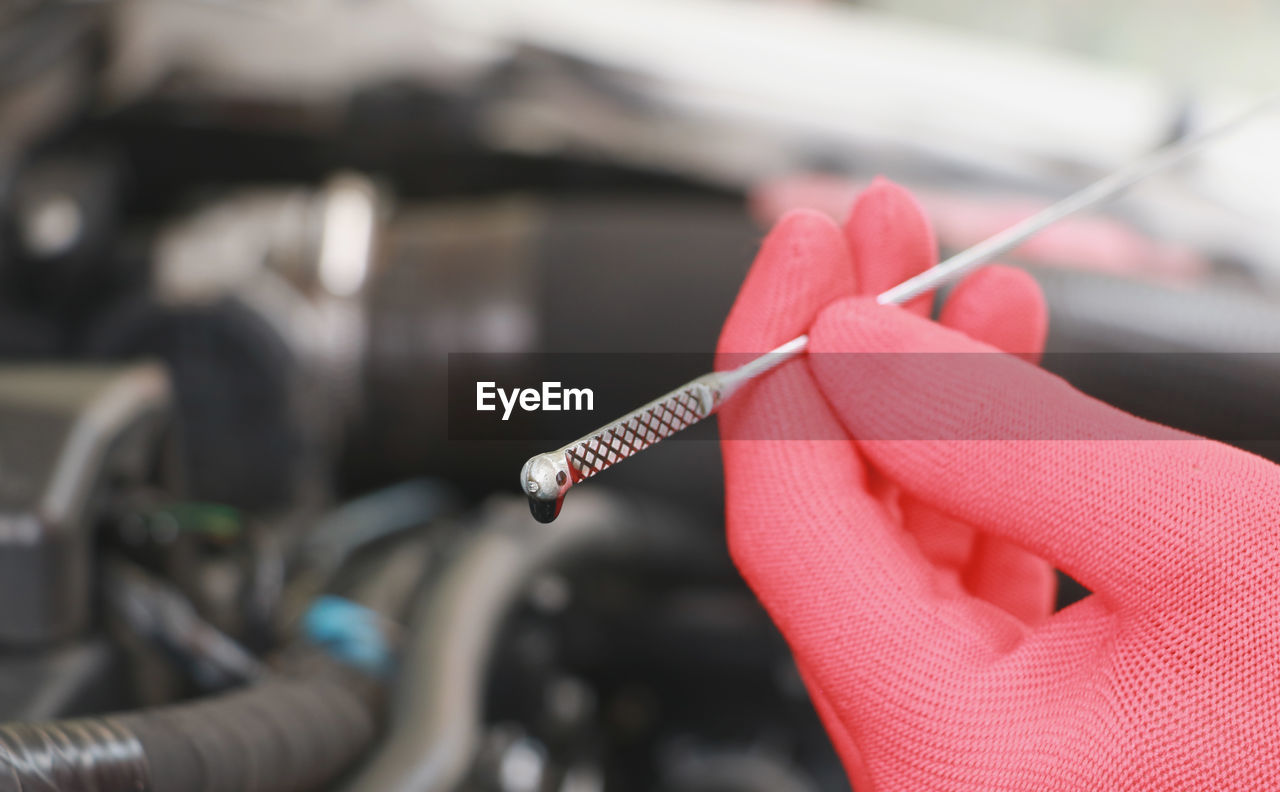 Close-up of hand holding tool against car engine in garage