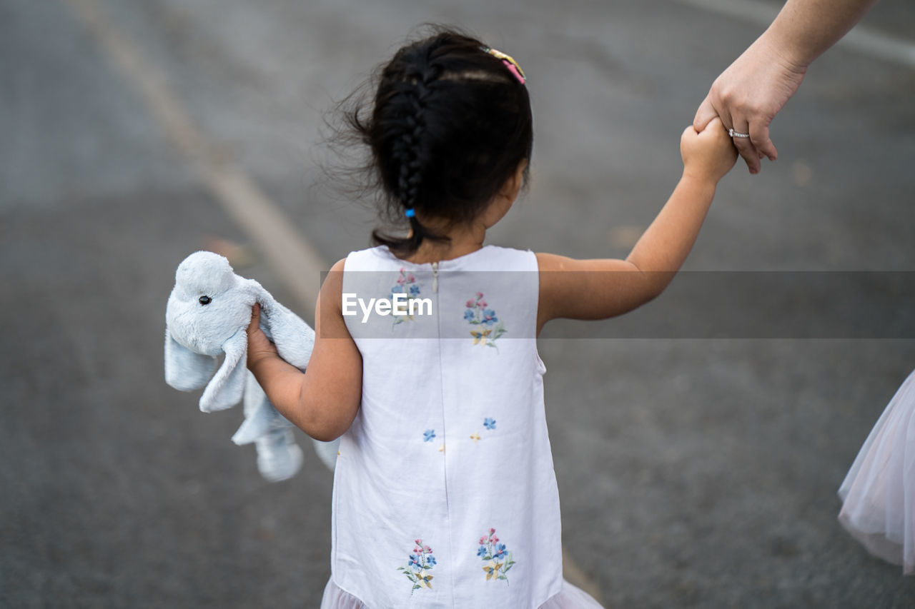 Girl holding dog doll walking at street with mum