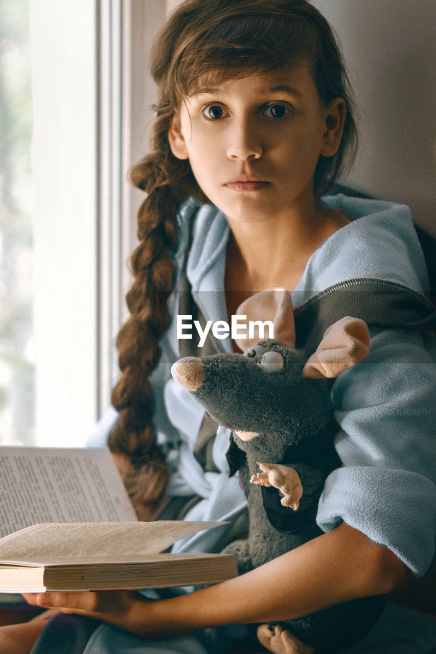 Portrait of girl with stuffed toy holding book at home