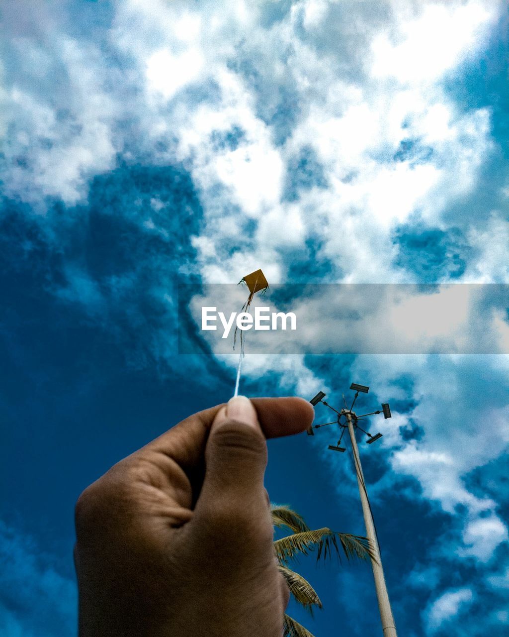 Close-up of hand holding kite string against blue sky