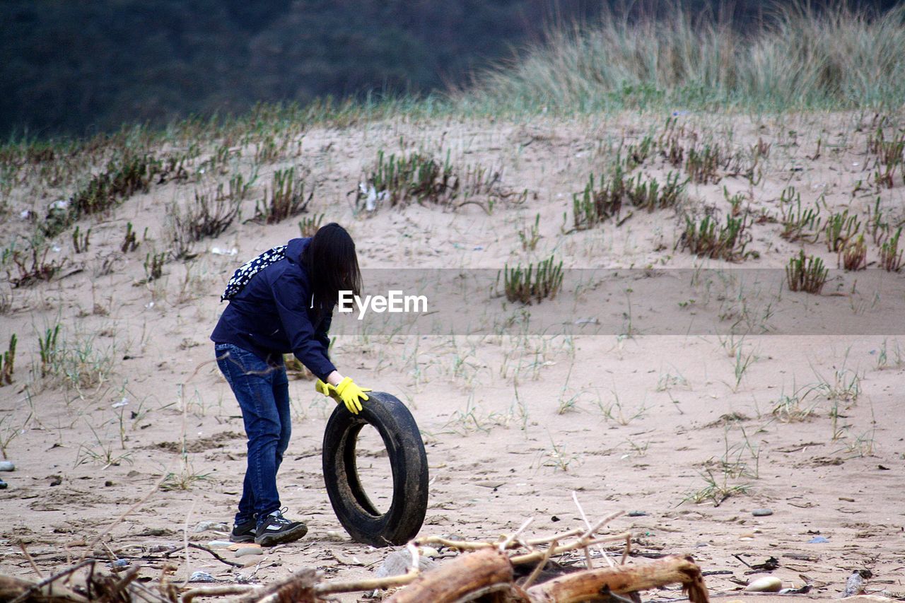 Woman rolling tire on sandy beach