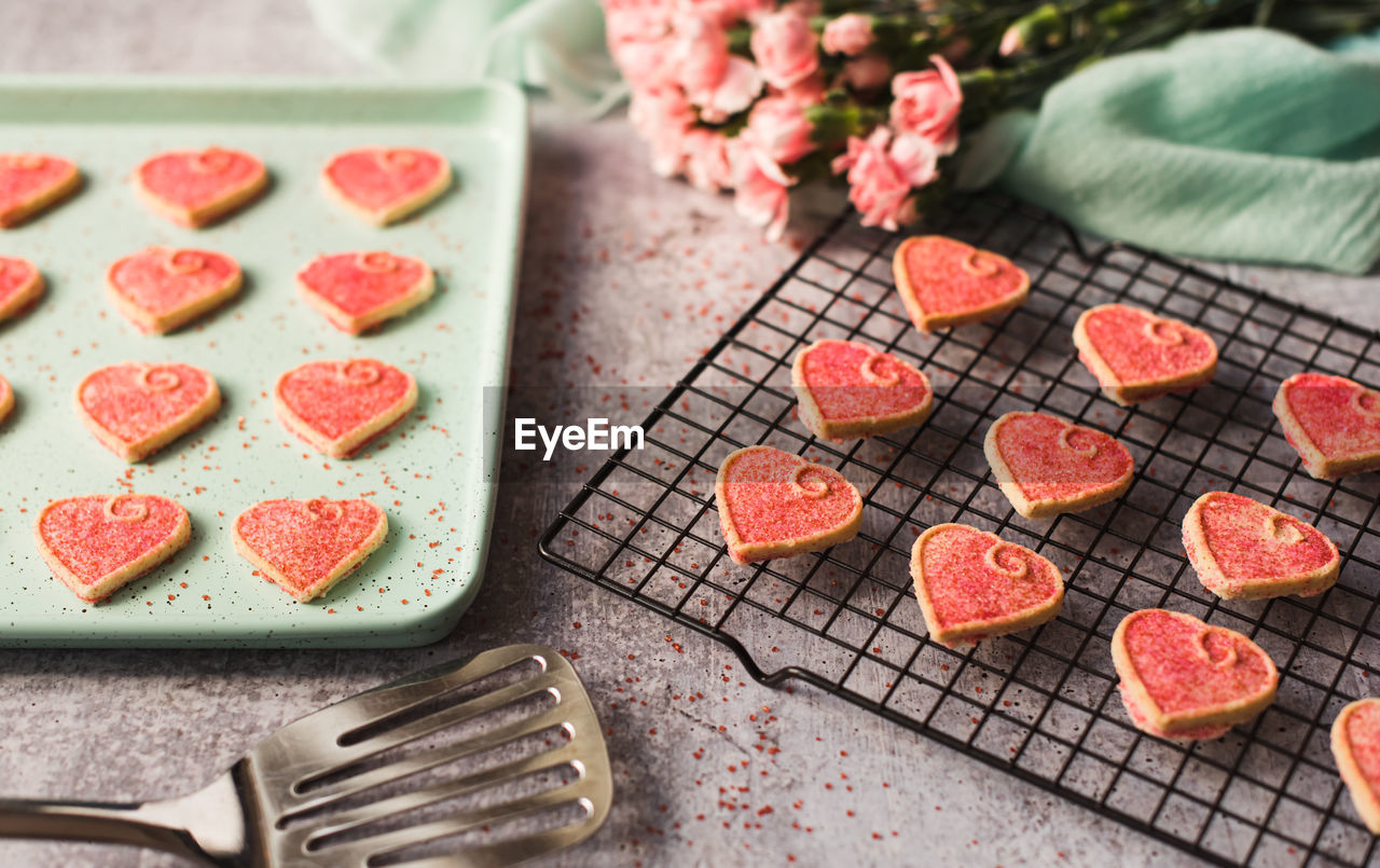 Pink valentine's day heart cookies cooling on a pan and rack.