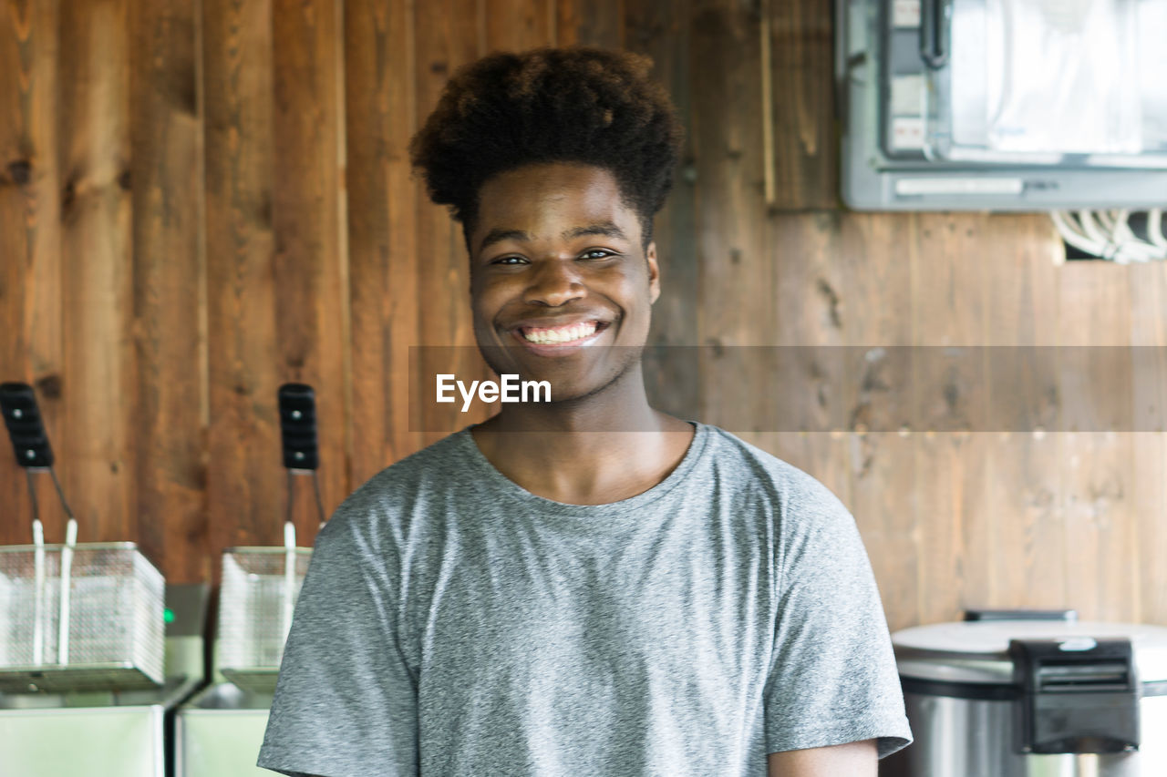 PORTRAIT OF SMILING YOUNG MAN STANDING AGAINST CURTAIN