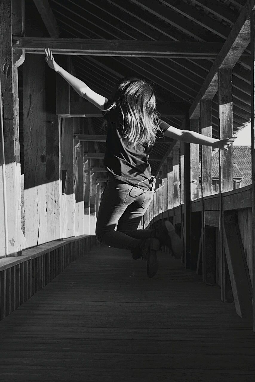 Rear view of woman jumping on footbridge