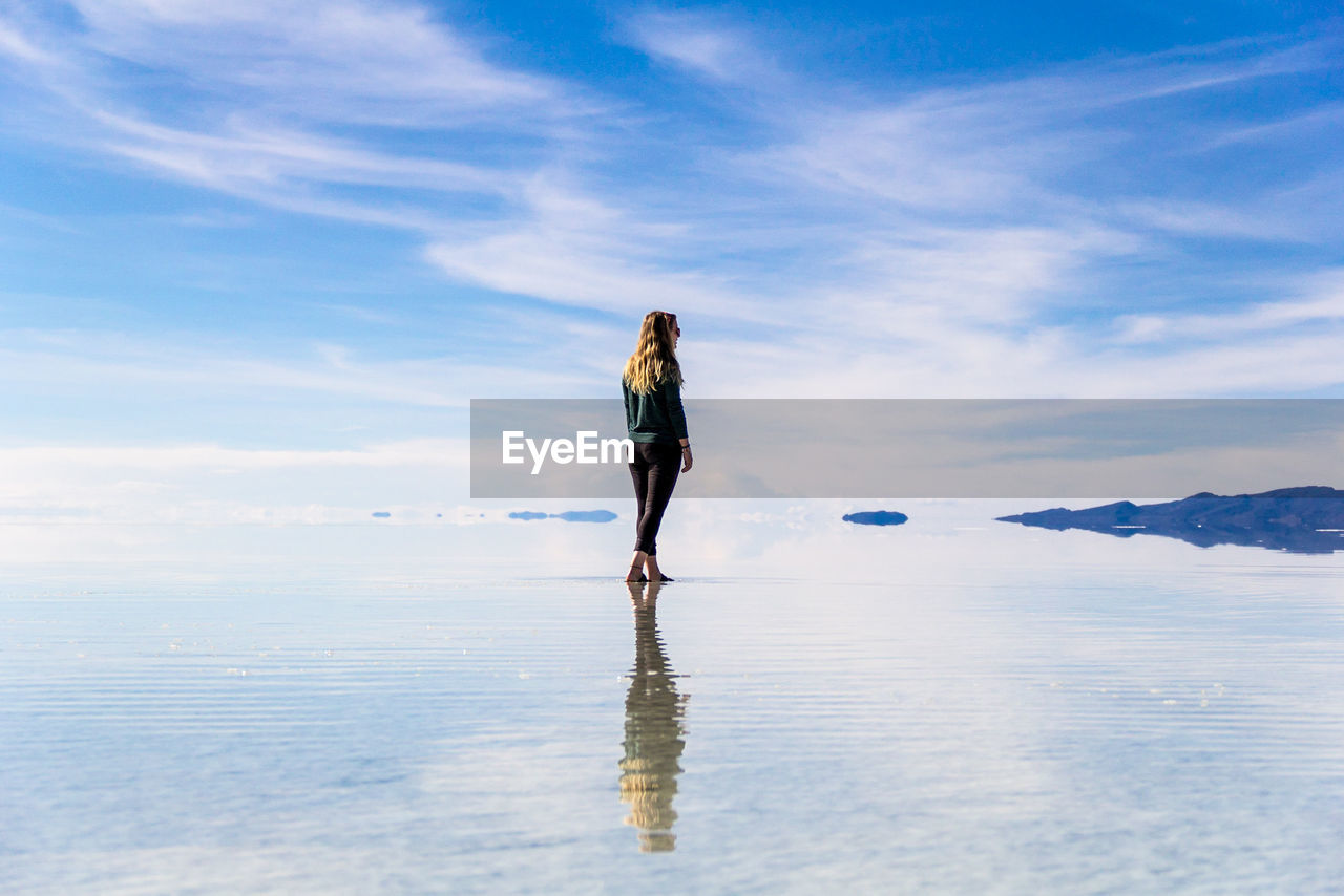 Rear view of young woman standing by infinity pool against cloudy sky