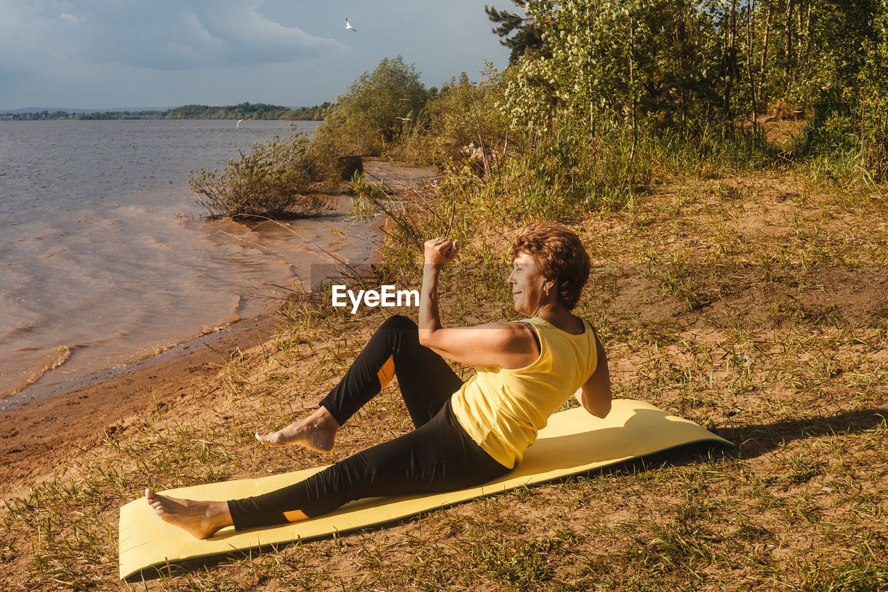 YOUNG WOMAN SITTING ON LAND BY WATER