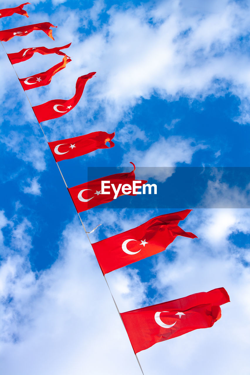 Many turkish national flags on rope against background of blue sky and clouds. vertical photo.