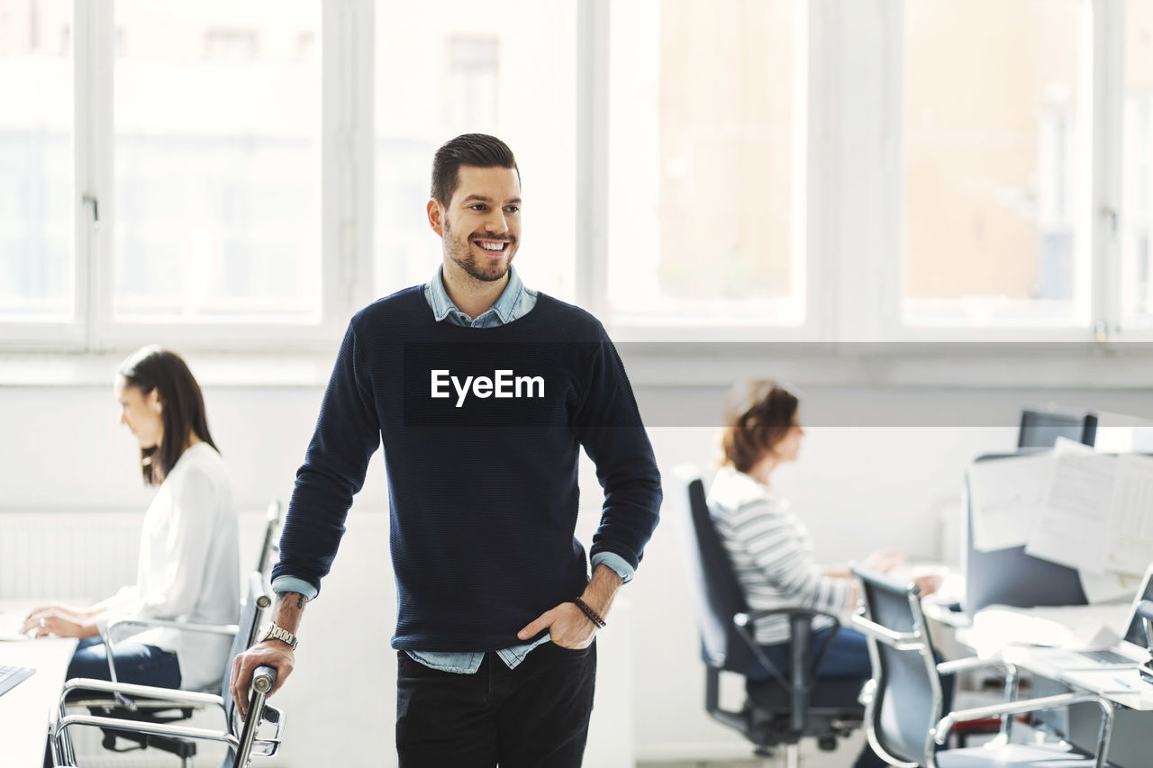 Happy mid adult businessman with colleagues working in background at office