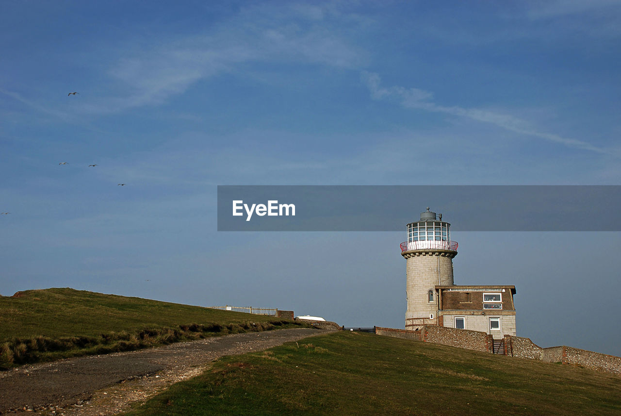 LIGHTHOUSE BY ROAD AMIDST BUILDINGS AGAINST SKY