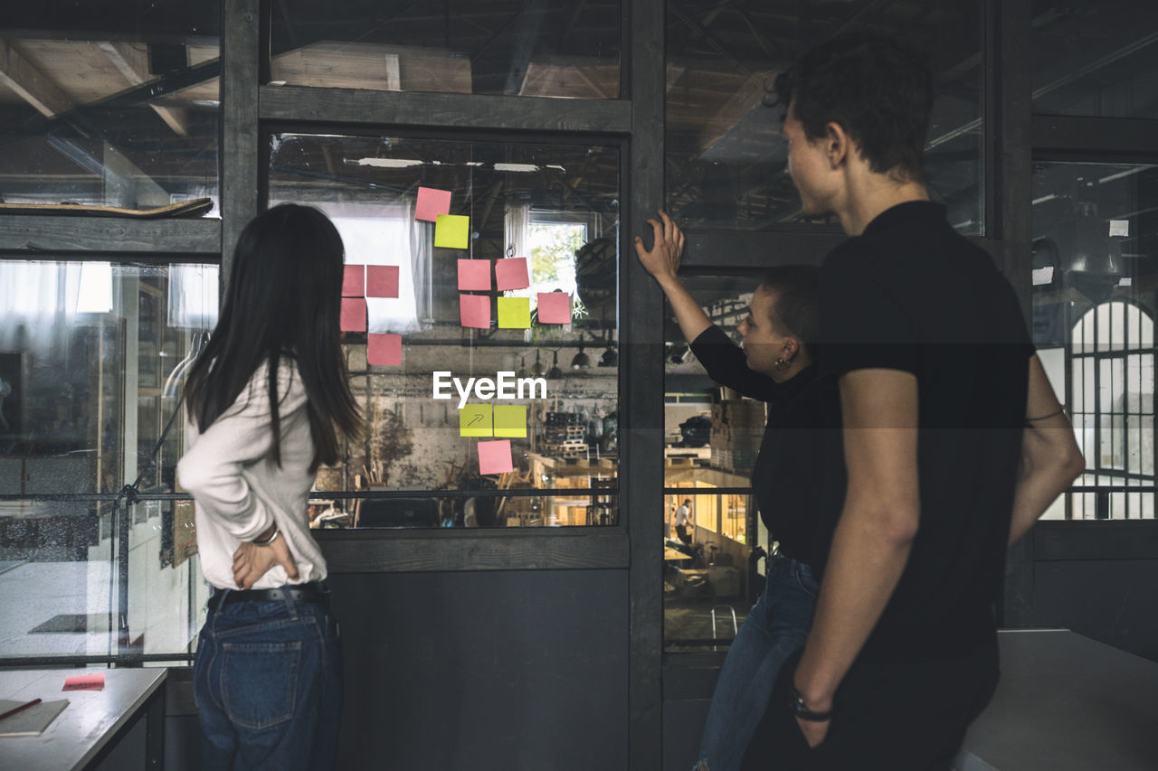 Male an female coworkers reading sticky notes on glass door at workplace