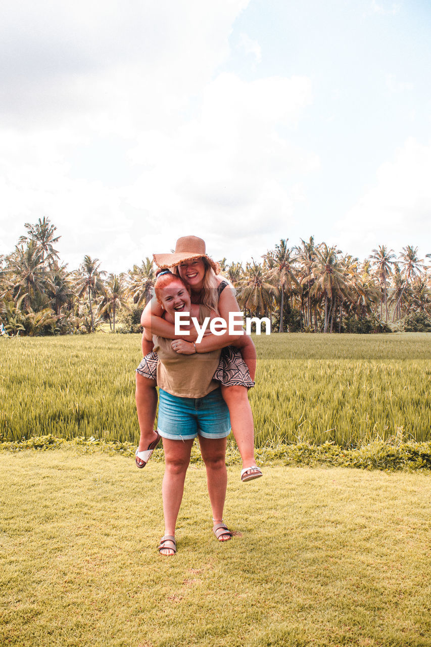 Portrait of happy friends standing on field against sky