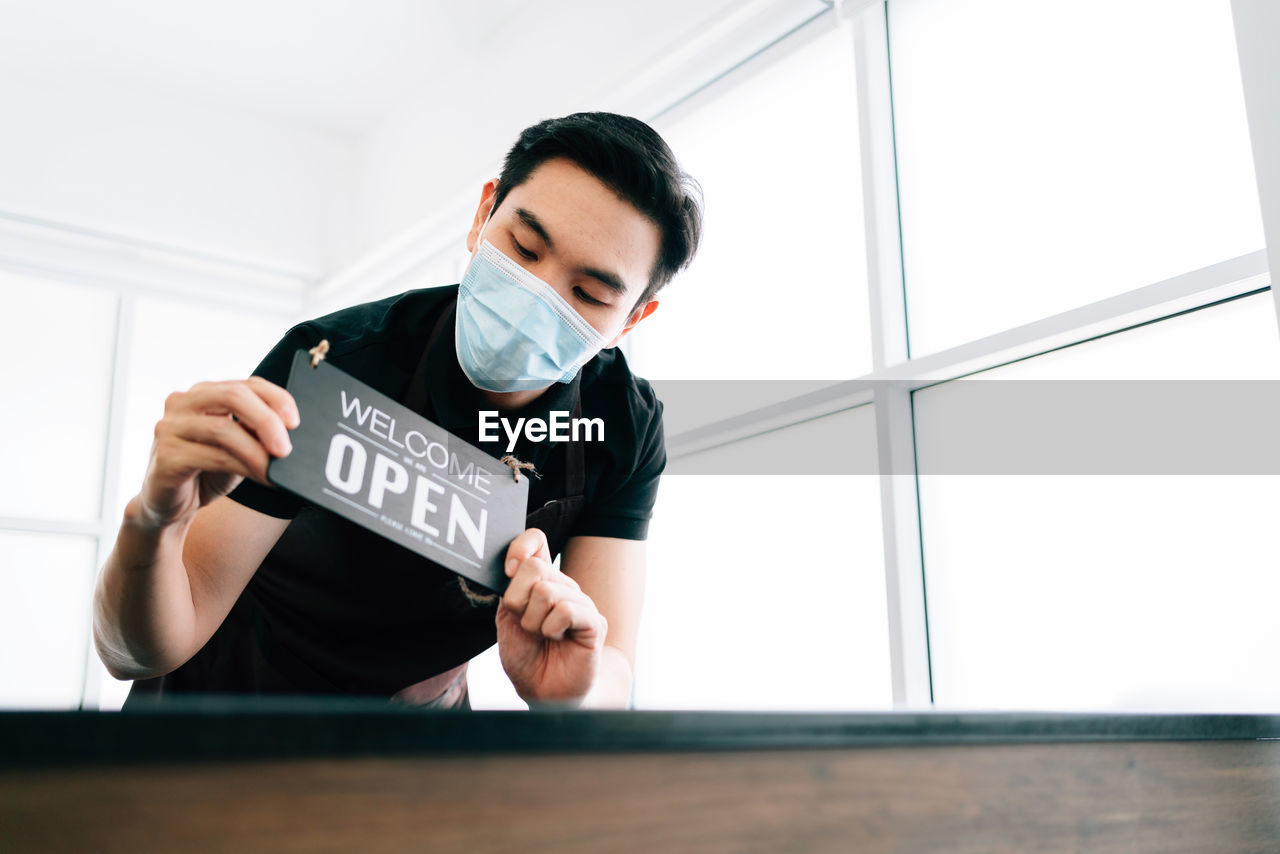 Man wearing mask holding open sigh against window