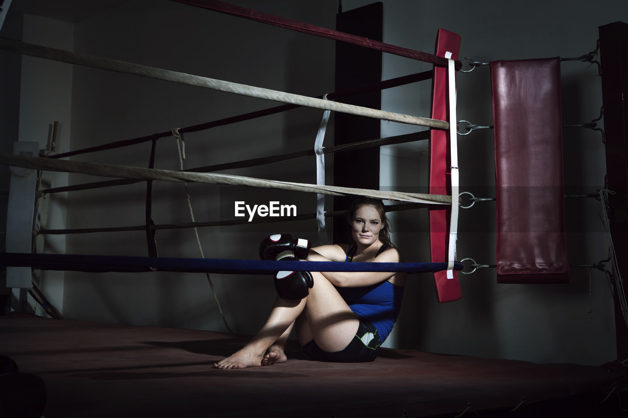 Tired sportswoman sitting in boxing ring at gym