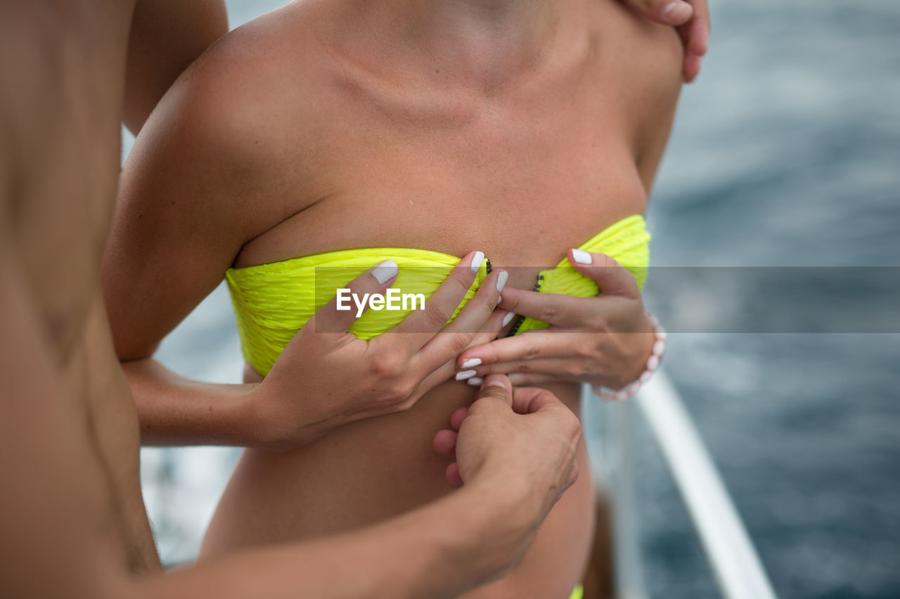 Cropped image of man unzipping woman bikini top