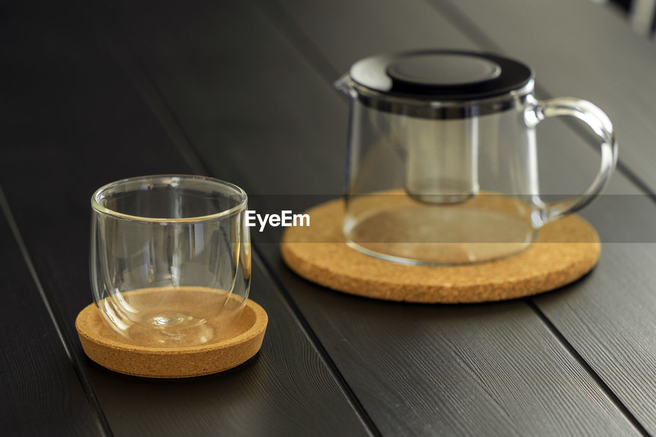 Empty modern glass tea cup with cork saucer and teapot over black dining table - horizontal.jpg