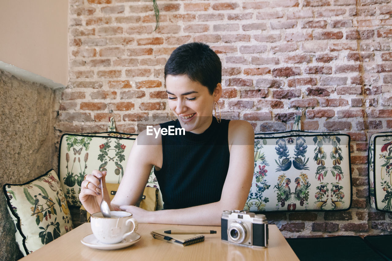 Young woman smiling while standing against brick wall