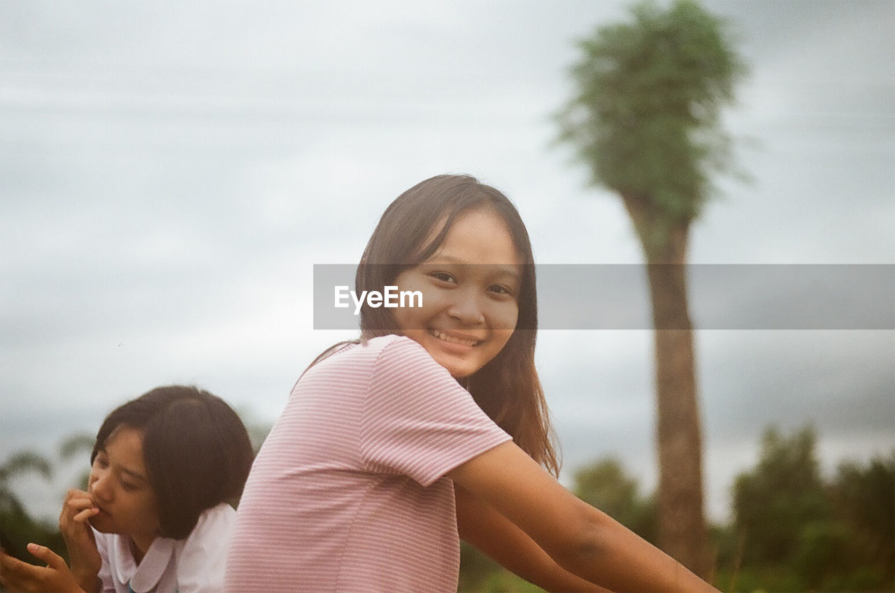 Portrait of smiling girl against plants and trees against sky