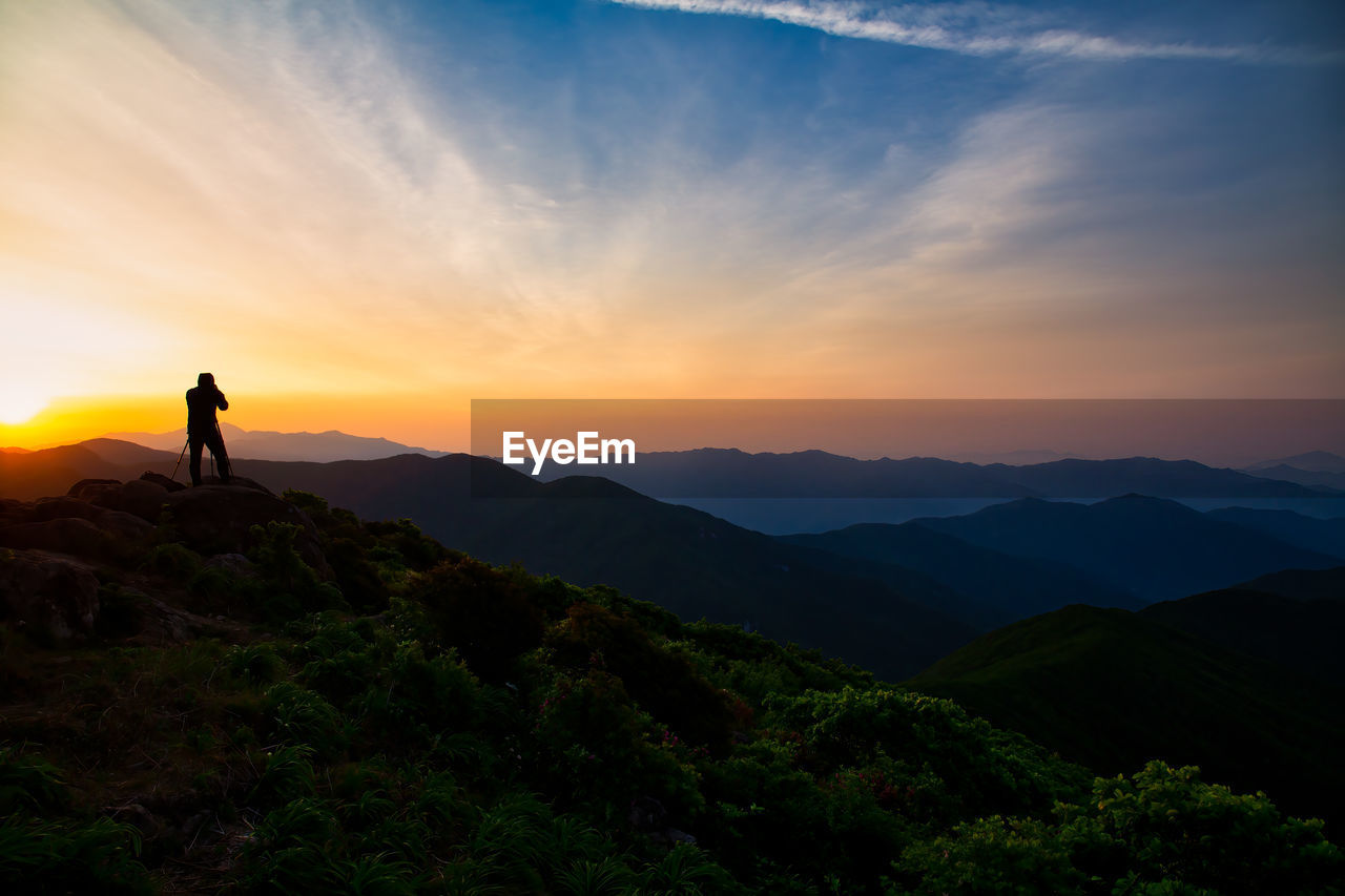 Rear view of man standing on mountain against sky during sunset