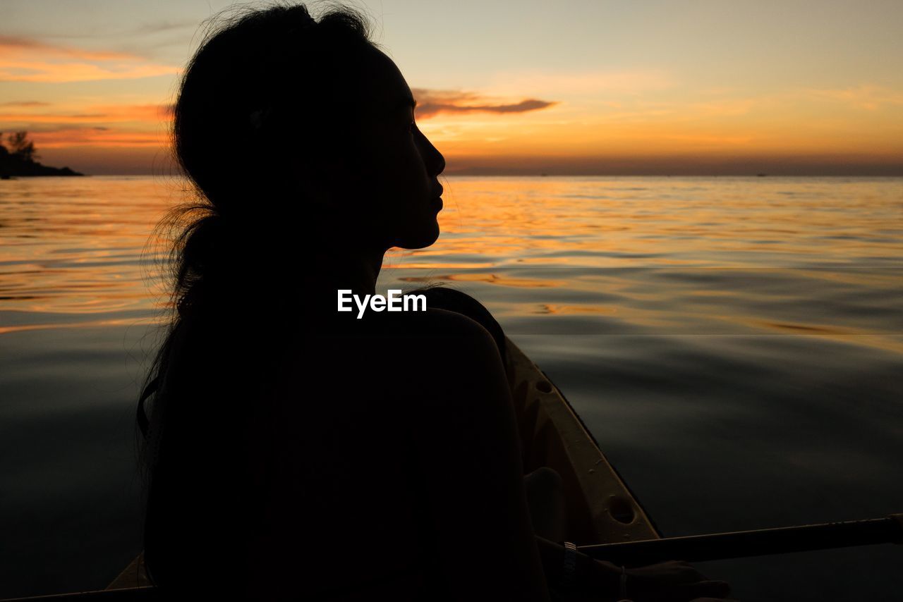 Silhouette woman sitting on kayak in sea against sky during sunset