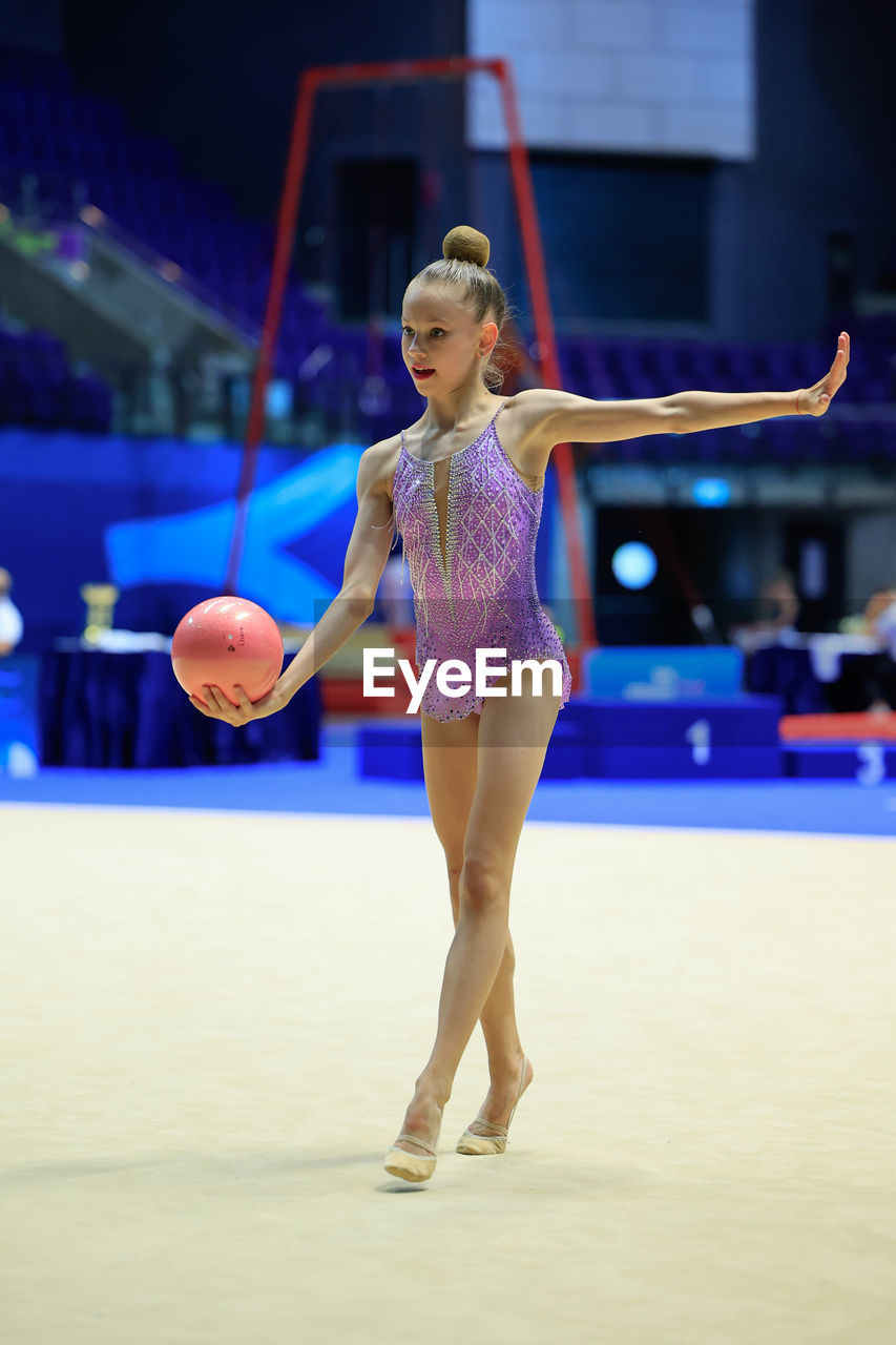 A rhythmic gymnast performs with a ball, displaying artistry and athleticism at a competition