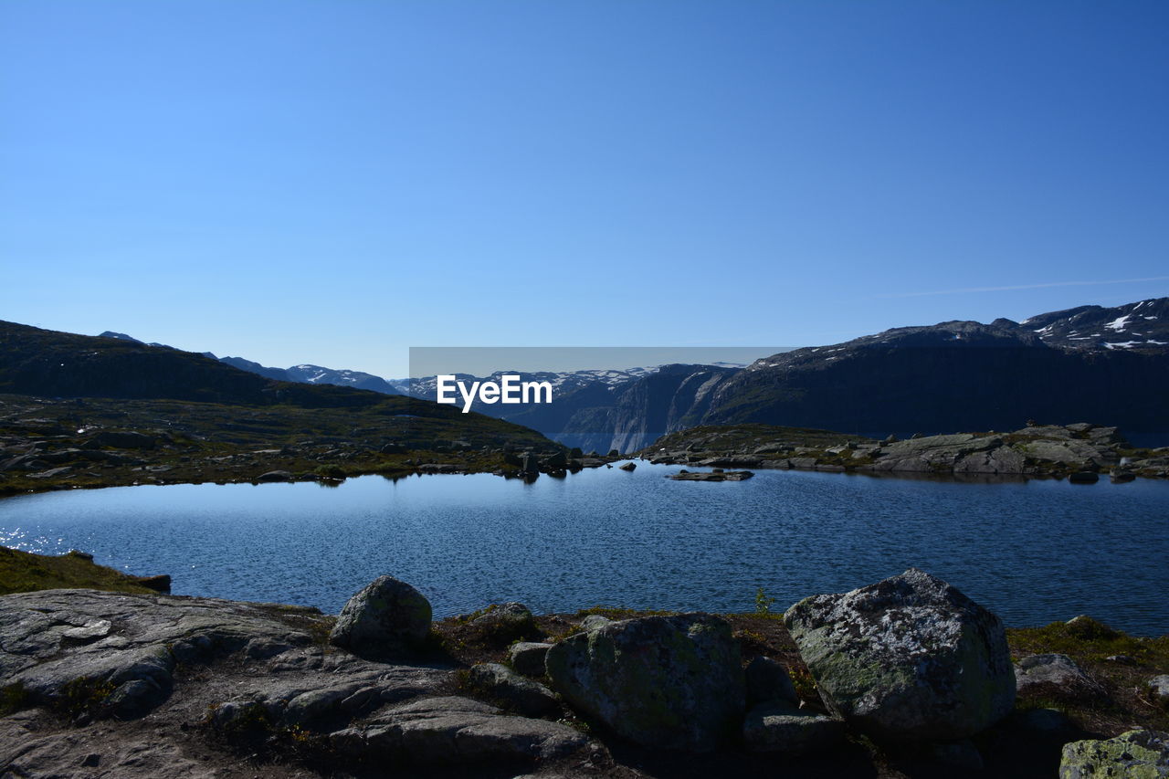 Scenic view of lake and mountains against clear blue sky