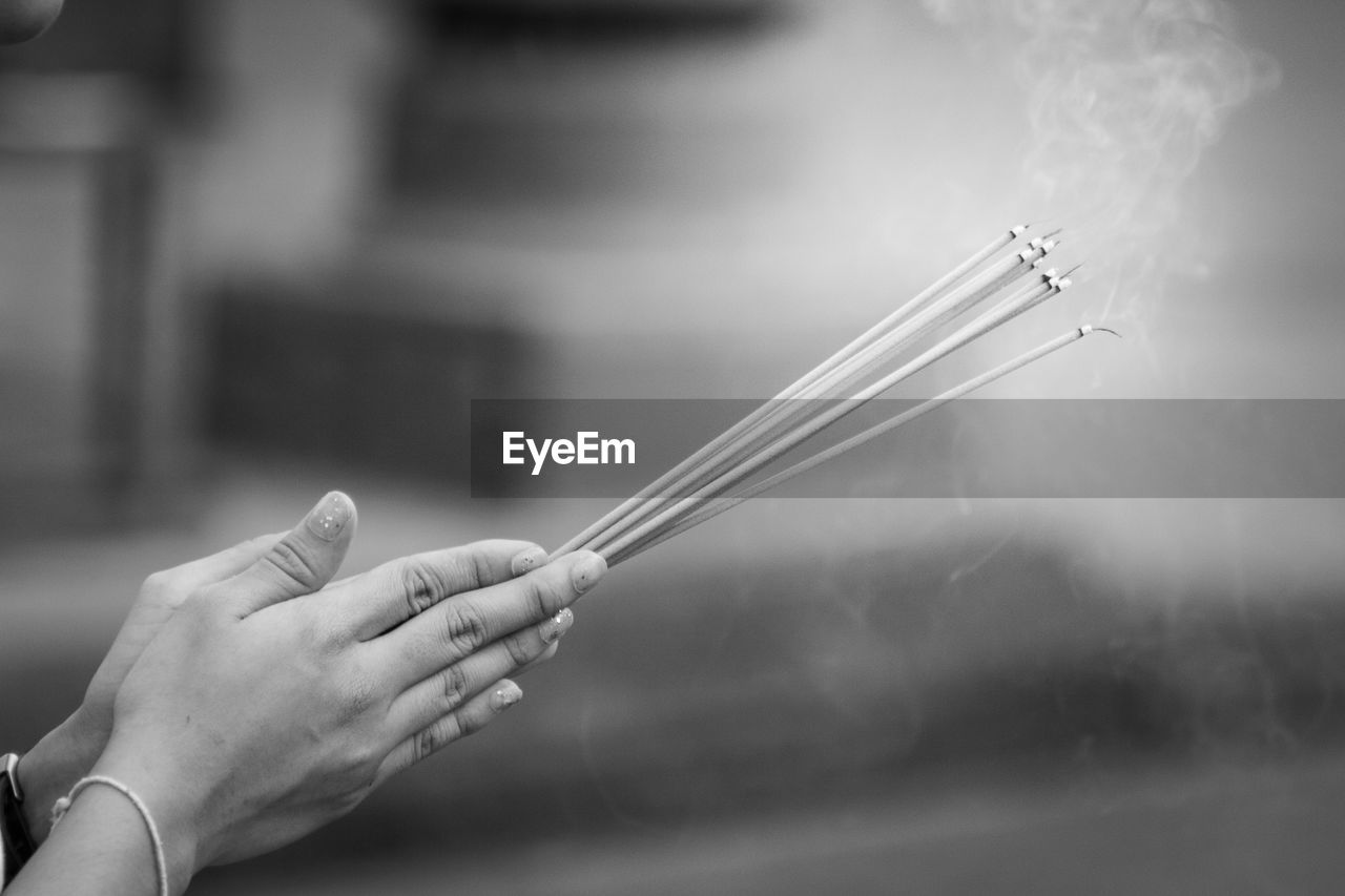 Cropped hands of woman holding lit incense sticks while praying at temple