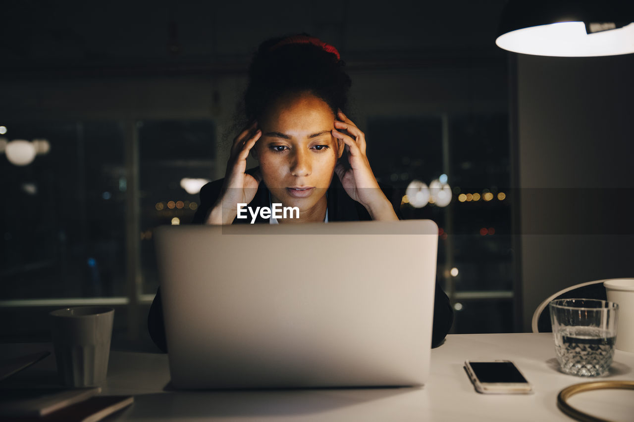 Young female entrepreneur with headache while working late in office