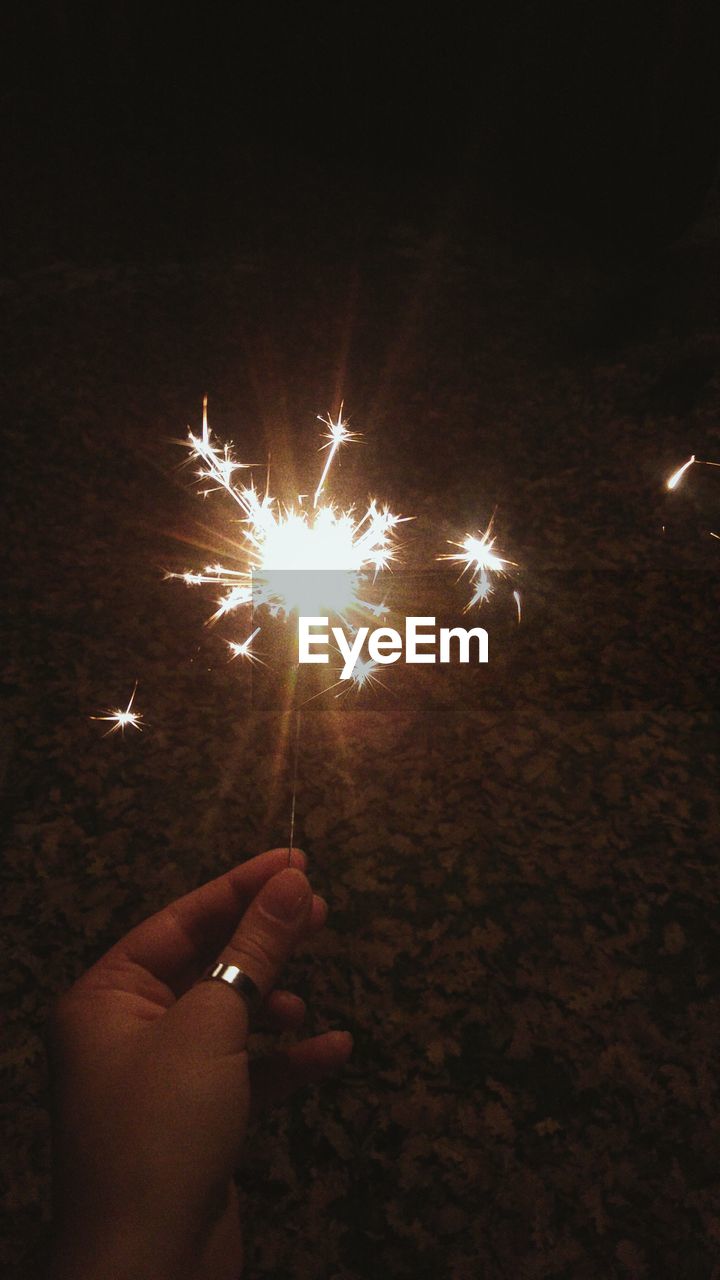 CLOSE-UP OF HANDS OVER ILLUMINATED FIREWORK DISPLAY