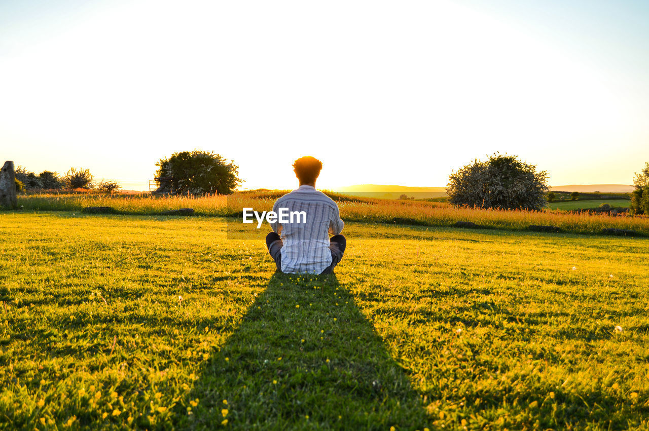 REAR VIEW OF MAN STANDING ON FIELD