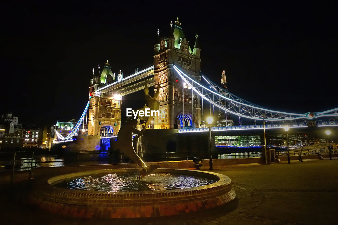 ILLUMINATED BRIDGE OVER WATER AT NIGHT