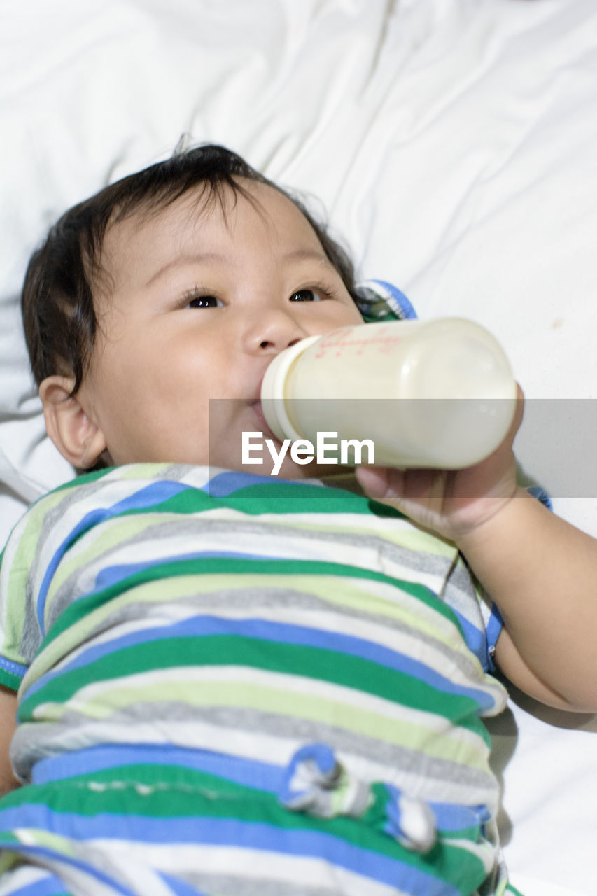 Baby girl drinking milk from milk bottle on bed at home